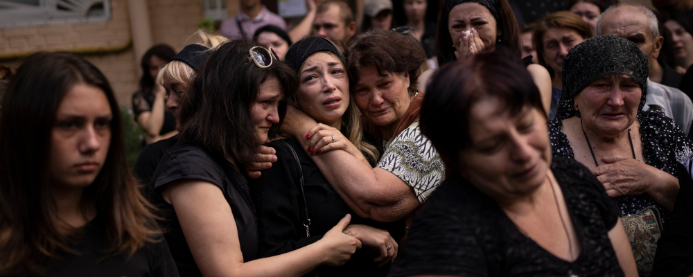 Anastasia Ohrimenko, 26, is comforted by relatives and friends as she cries next to a coffin with the body of her husband Yury Styglyuk, a Ukrainian serviceman who died in combat, during his funeral in Bucha, Ukraine, Aug. 31, 2022. Emilio Morenatti/AP Photo. 