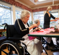 Inglewood Care Centre resident Connie Zweng, front left, paints a pine cone during arts and crafts recreation time as staff member Rita Horta, back, helps other residents at the long-term care home in West Vancouver, on Thursday, December 16, 2021. Darryl Dyck/The Canadian Press. 