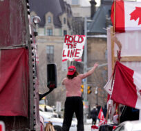 A protester dances on a barrier in front of vehicles and placards on Rideau Street, during a protest against COVID-19 measures, in Ottawa, on Wednesday, Feb. 16, 2022. Justin Tang/The Canadian Press. 