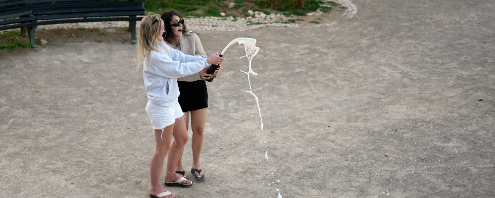 Two women open a bottle of sparkling wine at a public garden as night falls, in Lisbon, Portugal, Monday, July 3, 2023. Armando Franca/AP Photo. 
