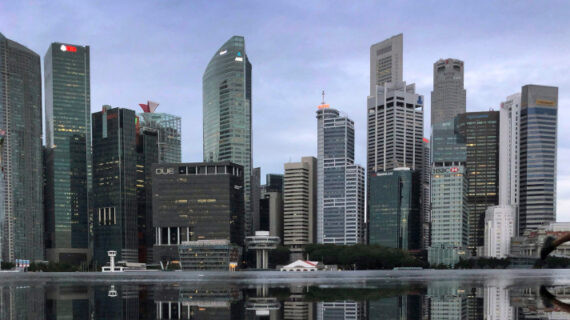 In this Thursday, Jan. 25, 2018, file photo, the financial skyline of Singapore is reflected in a rain puddle as people jog past at dawn. Wong Maye-E/AP Photo. 