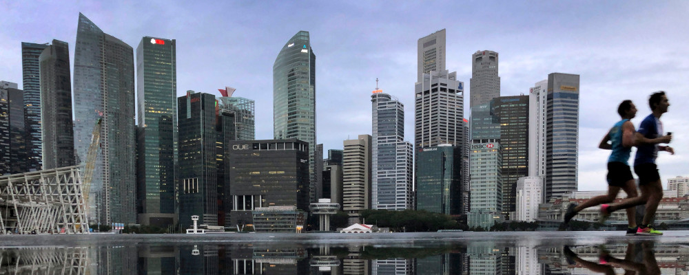 In this Thursday, Jan. 25, 2018, file photo, the financial skyline of Singapore is reflected in a rain puddle as people jog past at dawn. Wong Maye-E/AP Photo. 