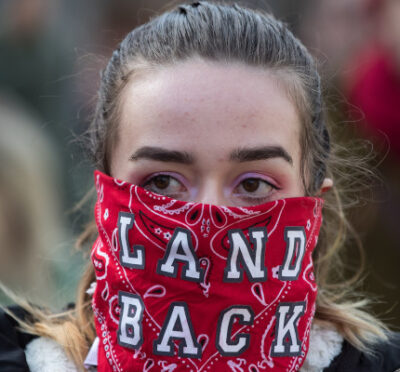 A woman wears a bandana over her face reading "Land Back" during a demonstration in Vancouver, on Monday, February 24, 2020. Darryl Dyck/The Canadian Press. 