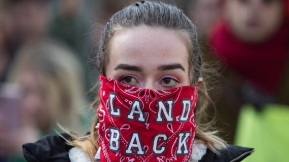 A woman wears a bandana over her face reading "Land Back" during a demonstration in Vancouver, on Monday, February 24, 2020. Darryl Dyck/The Canadian Press. 
