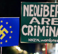 Protestors holds banners reading "neoliberals are criminals" and a EU flag with the nazi symbol on it during a demonstration outside Parliament as lawmakers debate budget spending cuts for 2013 in Madrid, Spain, Tuesday, Oct. 23, 2012. Andres Kudacki/AP Photo. 