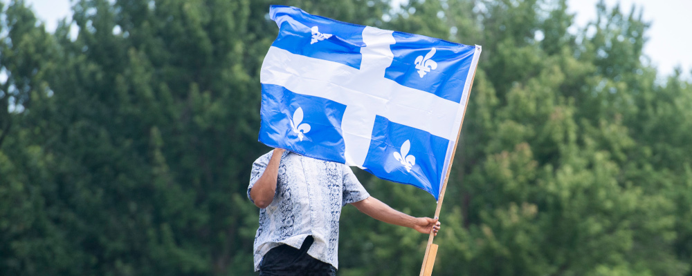 A man walks through a park with a Quebec flag on Saint-Jean-Baptiste Day in Montreal, Thursday, June 24, 2021. Graham Hughes/The Canadian Press. 
