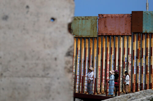 People walk along the wall that separates the United States from Mexico, near a slab of the Berlin Wall, in Tijuana, Mexico, Friday, Aug. 25, 2023. Gregory Bull/AP Photo.