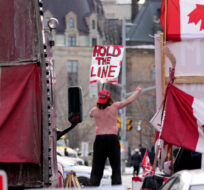 A protester dances on a concrete jersey barrier in front of vehicles and placards on Rideau Street during a protest against COVID-19 measures in Ottawa, on Wednesday, Feb. 16, 2022. Justin Tang/The Canadian Press. 