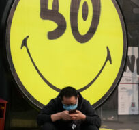 A man wearing a mask sits near a smiley face on Thursday, March 10, 2022, in Beijing. Ng Han Guan/AP Photo. 
