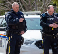 Two RCMP officers observe a moment of silence to honour slain Const. Heidi Stevenson and the other 21 victims of the mass killings at a checkpoint on Portapique Road in Portapique, N.S. on Friday, April 24, 2020. Andrew Vaughan/The Canadian Press. 