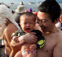A man holds his crying son after taking a dip in the frigid waters of English Bay during the 92nd annual Polar Bear Swim in Vancouver, B.C., on Sunday January 1, 2012. Darryl Dyck/The Canadian Press. 