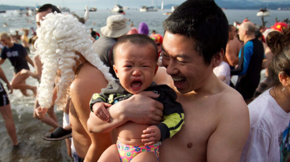 A man holds his crying son after taking a dip in the frigid waters of English Bay during the 92nd annual Polar Bear Swim in Vancouver, B.C., on Sunday January 1, 2012. Darryl Dyck/The Canadian Press. 